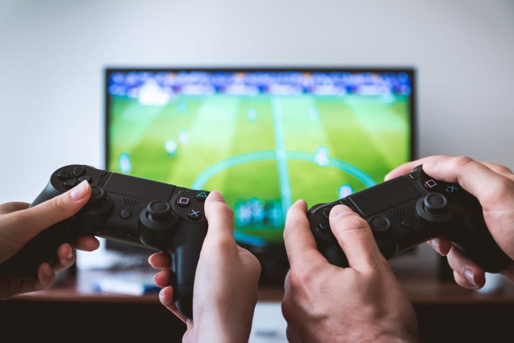 Image of hands playing two video game controllers in the foreground with a television farther away playing online gaming from an RV over mobile internet